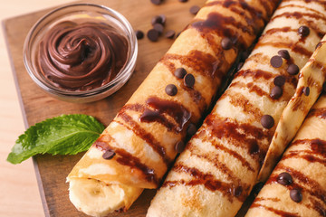 Delicious pancakes with chocolate sauce and banana on wooden board, closeup