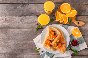 Delicious pancakes with orange and cranberry on wooden table