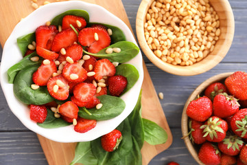 Plate of salad with spinach, strawberry and pine nuts on board