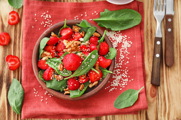 Plate of salad with spinach, strawberry and walnuts on table