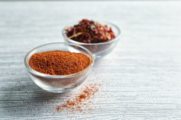 Chili powder and flakes in bowls on wooden table