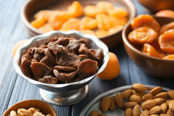 Dried apricots and nuts in different dishes on wooden table