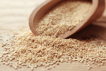 Closeup of scoop with raw quinoa grains on wooden table