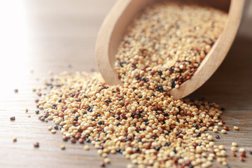 Closeup of scoop with raw quinoa grains on wooden table
