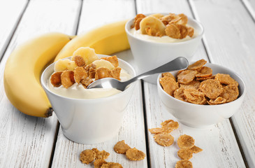 Bowls with yummy banana pudding and flakes on wooden table