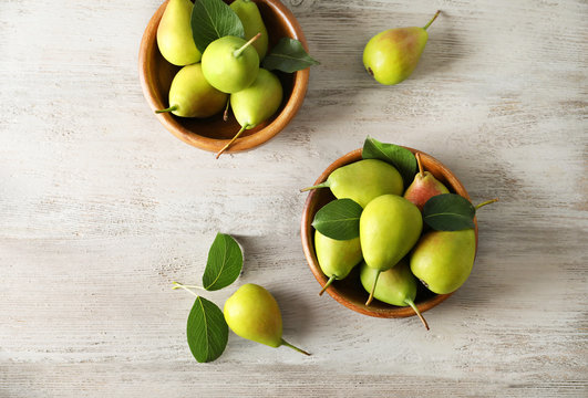 Ripe pears in bowls on wooden background