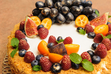 Beautiful large honey cake decorated with fruits and berries on top with pears and sea buckthorn  gold kandurin, grapes, figs, kumquat, on a wooden table. 