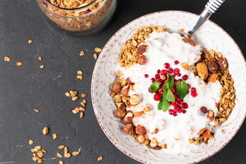 Granola with yoghurt, blueberries and blackberries in a white plate on a black background, selective focus, horizontal
