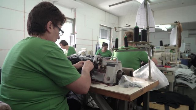 Group of professional female tailors work in workshop, mature woman demonstrates her skills by sewing machines and scissors to stitches clothes, women tailoring fabric textiles, dolly shot, room inter
