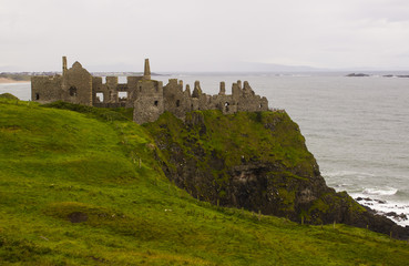 Fototapeta na wymiar The shadowy ruins of the medieval Irish Dunluce Castle on the cliff top overlooking the Atlantic Ocean on the north coast of Ireland. Taken on a dull wet day