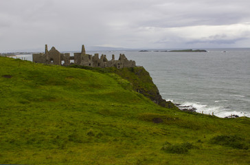 Fototapeta na wymiar The shadowy ruins of the medieval Irish Dunluce Castle on the cliff top overlooking the Atlantic Ocean on the north coast of Ireland. Taken on a dull wet day