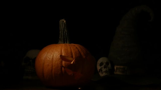 Carved Halloween pumpkin lights inside with flame and skuls around.