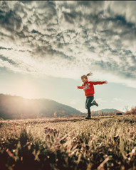 Portrait of a girl in a bucolic context, running in a field. Trees and hills in the background.