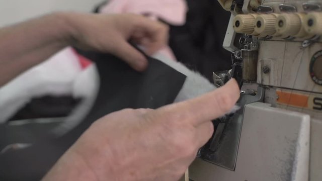 Tailoring close up, hands of elderly woman during works for sewing machine, female tailor stitching fabric textile, shallow depth of field, concept clothing factory, indoors, active scene