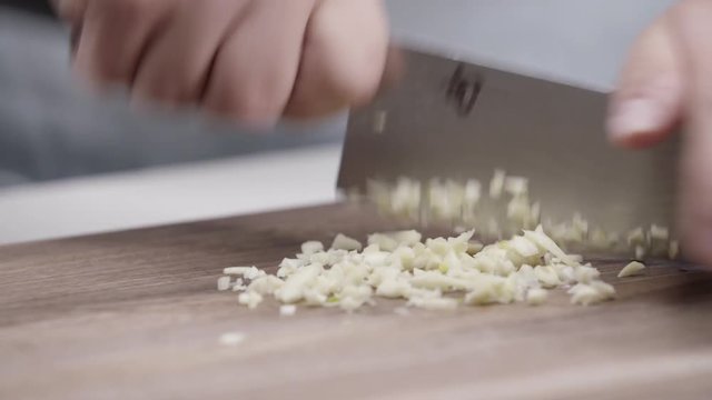 Close up, chef dices garlic on cutting board