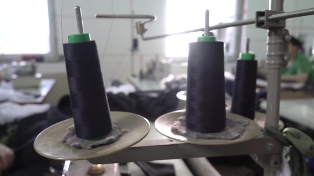 Dolly shot and focus change from the spool threads close up on female dressmaker during works at sewing machine, concept tailoring in clothing factory, room interior