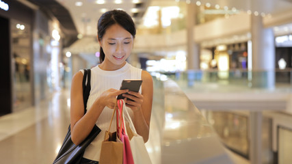 Woman looking at mobile phone and holding shopping bags in shopping center