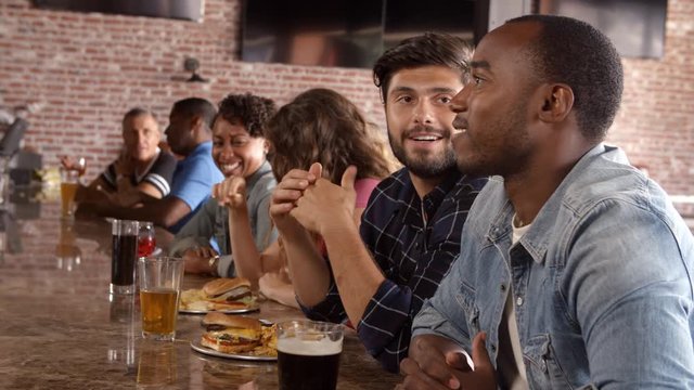 Group Of Friends Watching Game In Sports Bar On Screens