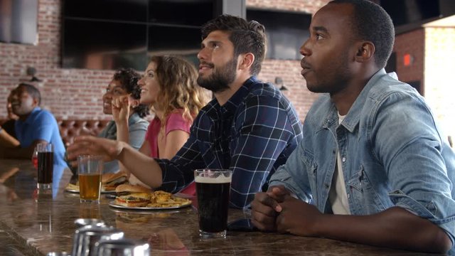 Group Of Friends Watching Game In Sports Bar On Screens