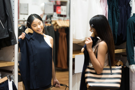 Young Asian Woman with Shoulder Bag Looking at Clothes Hanging on the Rail Inside the Clothing Shop.