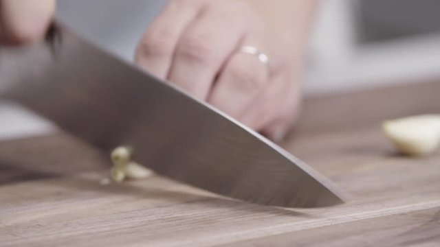 Person dices cloves of garlic on cutting board, close up