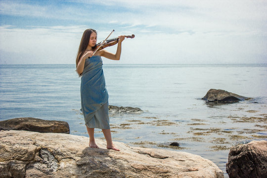 girl in blue playing violin by ocean