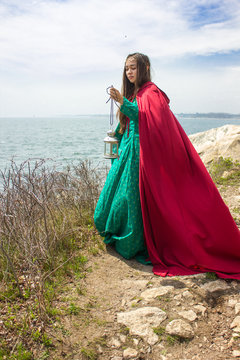 girl by ocean with lantern and red cape