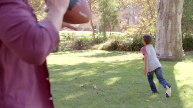 Dad and son passing American football to each other in park