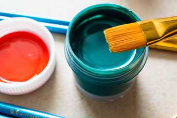 Plastic jar with green acrylic paint and brush above.