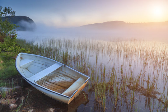 Boat on the shore of a misty lake on a summer morning
