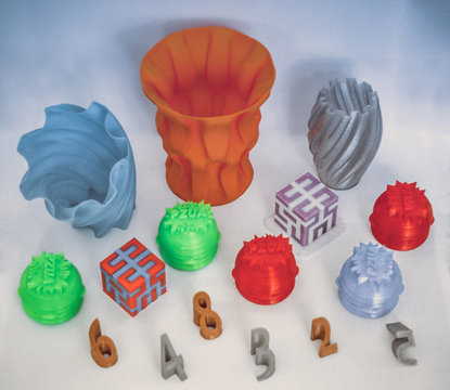 Models printed by 3d printer. Bright colorful objects printed on 3d printer on table.Automatic three dimensional printer performs plastic modeling in laboratory. Progressive modern additive technology