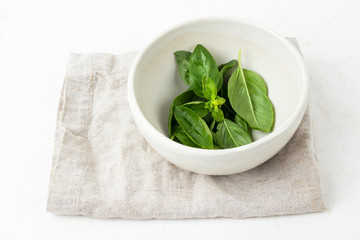 green basil in a white mortar on a napkin.