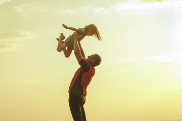 The happy father is lifting daughter up on the background of the evening sky