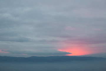 Red sunset filtering through an hole in the overcast sky, with mist filling a valley below