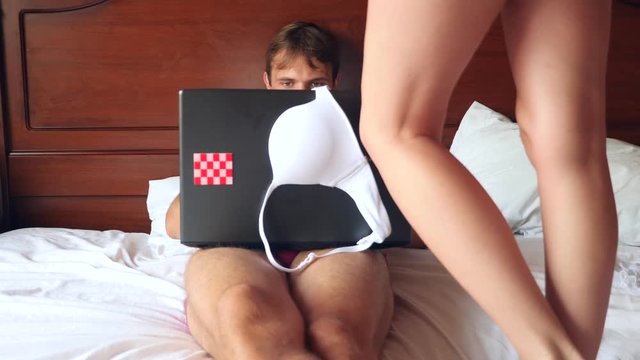 Sexy woman trying to seduce man working on laptop in bed. the girl takes off her underwear in front of her boyfriend, and he ignores her, works on a laptop. 4k, slow motion