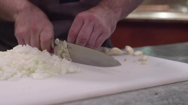 Close up, chef minces garlic on cutting board