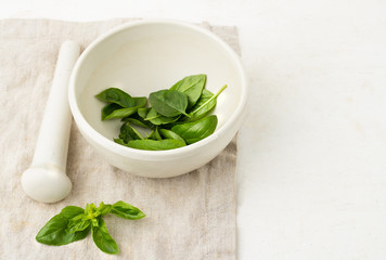 basil leaves in a white mortar on a napkin.