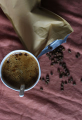 Coffee cup in white pottery mug, scattered coffee beans from paper package