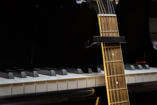 acoustic guitar with capo against grand piano keys - closeup musical instruments concept for musical composition and creativity