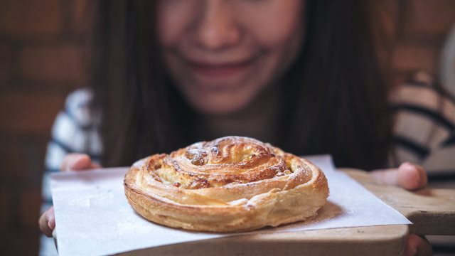Closeup image of a beautiful Asian woman holding and showing a raisin danish on wooden vintage table in bakery shop