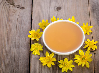 honey in the glass bowl and yellow flowers around it on wooden background