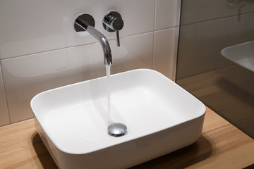 Close up of sink and faucet on wooden shelf in white bathroom interior