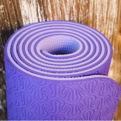 Close up of rolled lilac exercise mat on wooden background.Yoga accessories concept. Shallow depth...