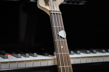 bass guitar against grand piano keys with plectrum - musical instruments closeup - concept musical...