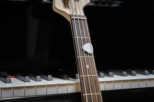 bass guitar against grand piano keys with plectrum - musical instruments closeup - concept musical composition and creativity