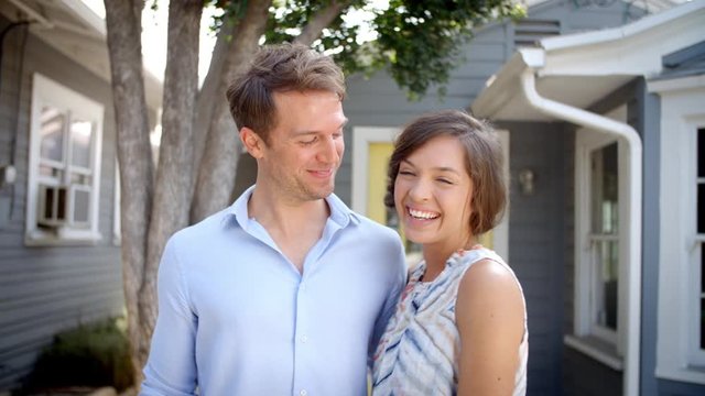 Portrait Of Happy Couple Standing Outside New Home With Keys