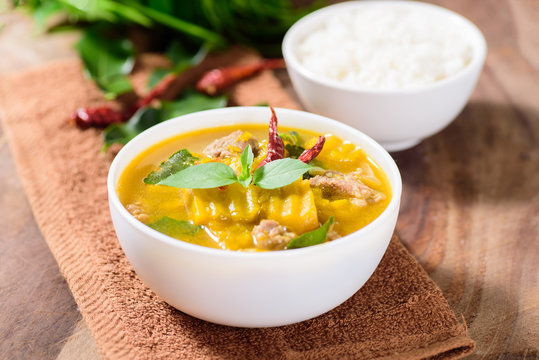 Thai food.Spicy pumpkin soup with pork and cooked rice in a bowl on brown fabric and wooden background