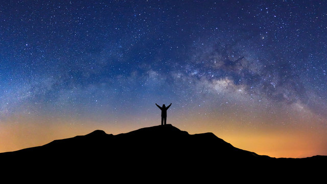 Fototapeta Panorama landscape with milky way, Night sky with stars and silhouette of a standing sporty man with raised up arms on high mountain.