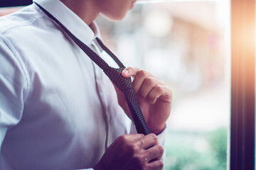 The businessman ties a black tie, in white shirt.