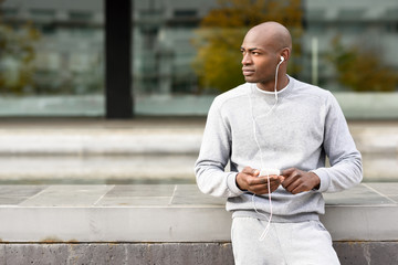 Attractive black man listening to music with headphones in urban background.